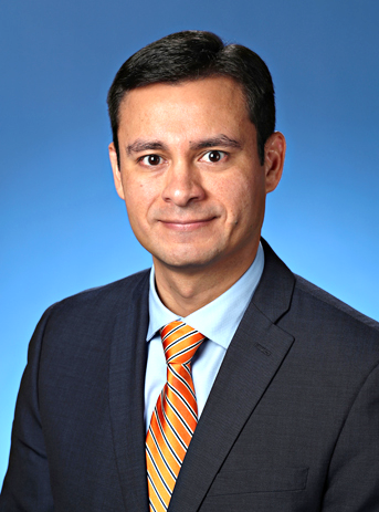 professional headshot of white male wearing a black suit jacket and orange tie against a blue background