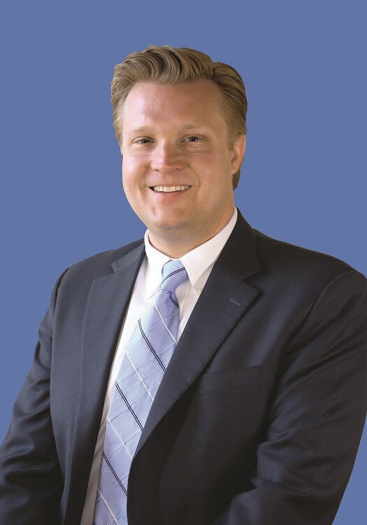 professional headshot of white male with blonde hair wearing a black suit jacket and blue tie against a blue background